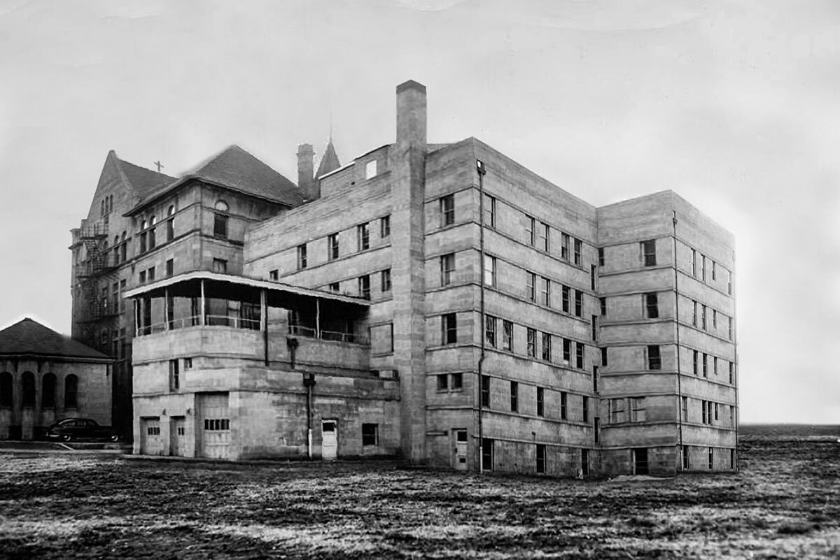 Faculty Hall is shown in 1952. The concrete brick building has five floors of rectangular windows with chimneys and shorter sections protruding. The area surrounding the building is lined with dirt and gravel.