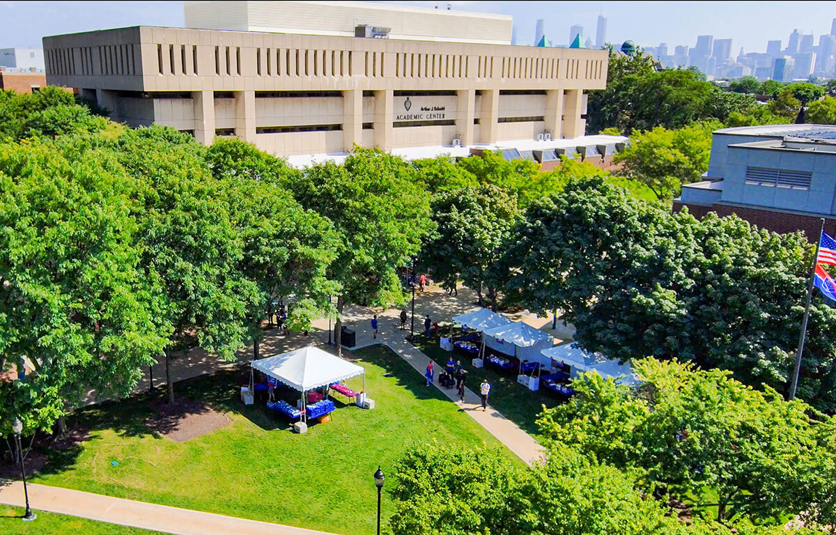 A grassy lawn with white tents and two intersecting concrete sidewalks is surrounded by green leafy trees, shown during the Blue Demon Welcome event in September 2022. Formerly a parking lot, the Quad now plays host to events and student gatherings, as well as being used as a study and meeting space.